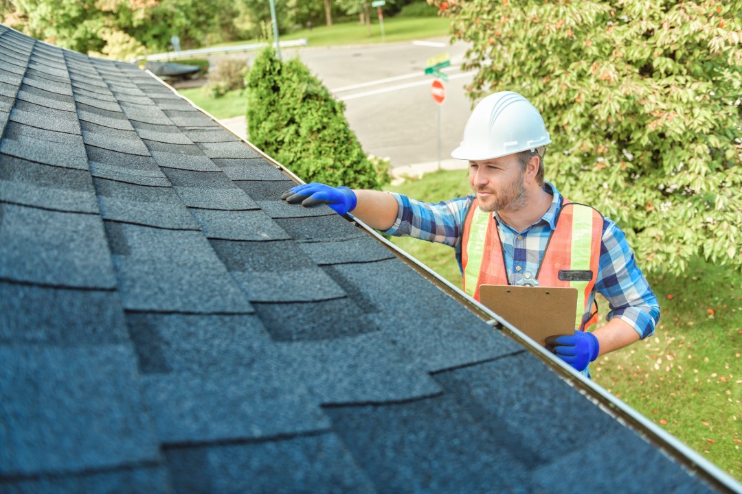 A man with hard hat standing on steps inspecting house roof