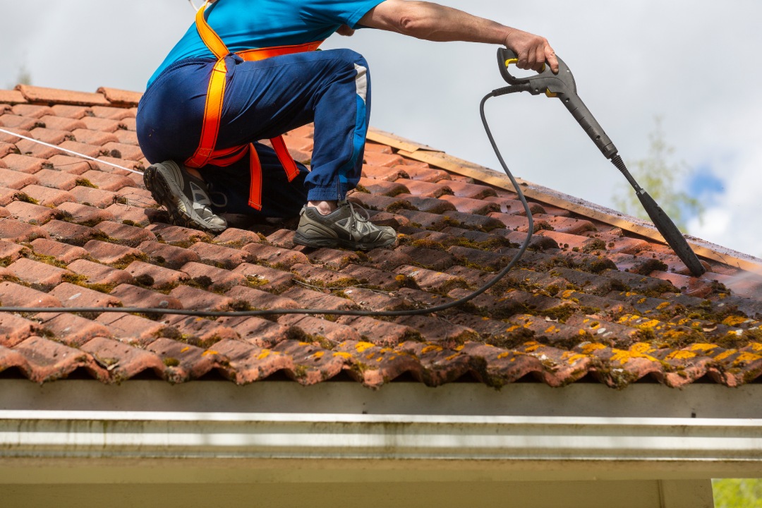 Man is washing the roof from moss with a high pressure washer. House maintenance work.